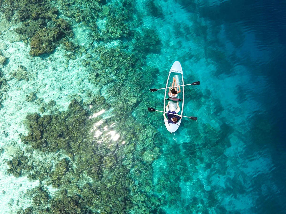 Aerial view of two kayakers paddling over a vibrant coral reef in turquoise Caribbean waters