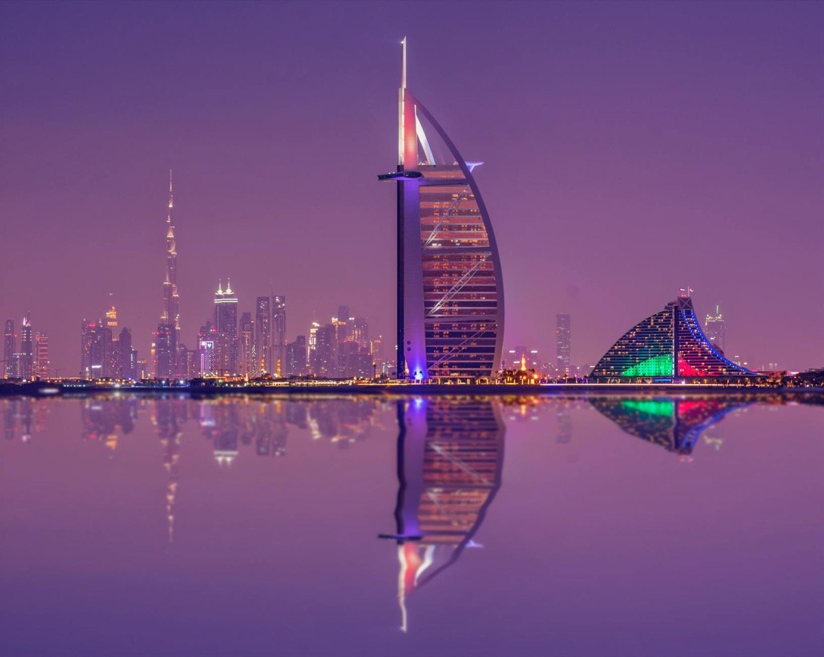 Dubai skyline at night with Burj Al Arab sail-shaped hotel and Burj Khalifa reflected in the water