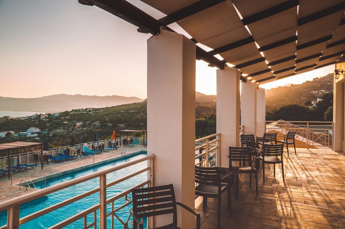 Luxury resort pool terrace with bar stools and pergola overlooking a hillside and sea at golden hour sunset